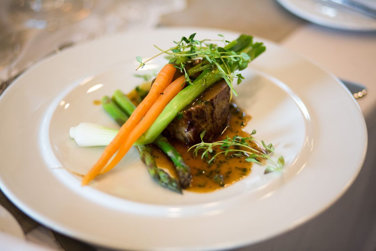 Plated main course of seared meat with glazed carrots and asparagus on a white plate