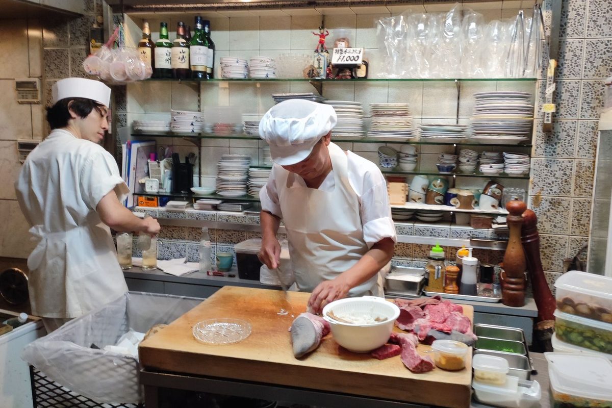 Two chefs plating dishes at the pass in a busy restaurant kitchen