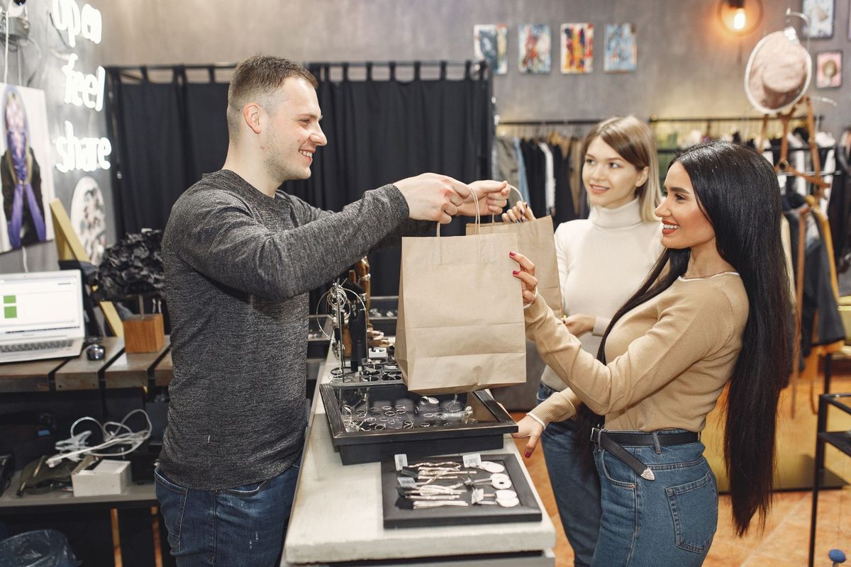 Small business owner handing a purchase to two happy customers in their shop